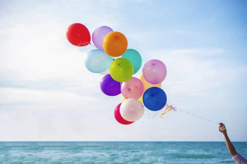 Dłoń trzymająca kolorowe balony, w tle widoczne niebo i morze.
